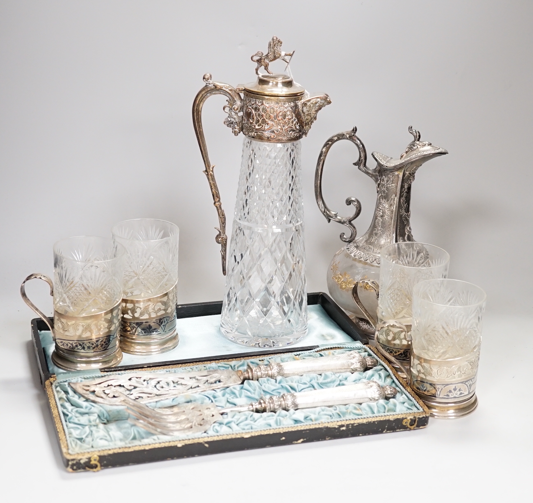 Two claret jugs, one with gilt decoration, four silver plated cup holders with glass liners and silver plated fish servers, the largest 32cm high